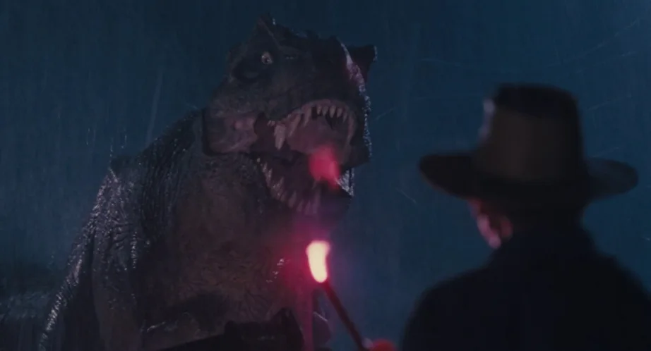 Alan Grant holding a flare in the rain, face to face with the T-rex